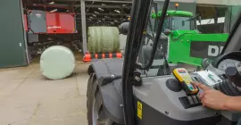 Távvezérlővel vezérelt RW 1110 egy istálló előterében, a háttérben etetőrobot látható.