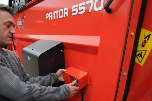 A KUHN PRIMOR 5570 M szalmakifúvó és takarmánykiosztó hátsó lenyíló csapóajtajának és az alsó behordópályának kihelyezett vezérlője a gép bal hátsó részén található