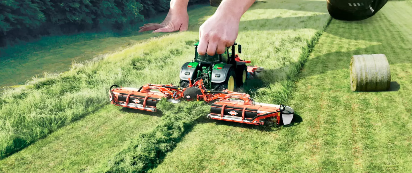 A giant sized farmer mows a field with a small tractor and mower